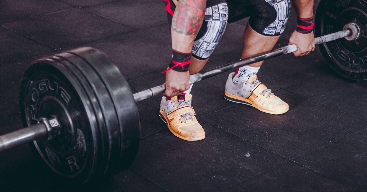 A lifter wearing weightlifting shoes while gripping a loaded barbell that's on the floor