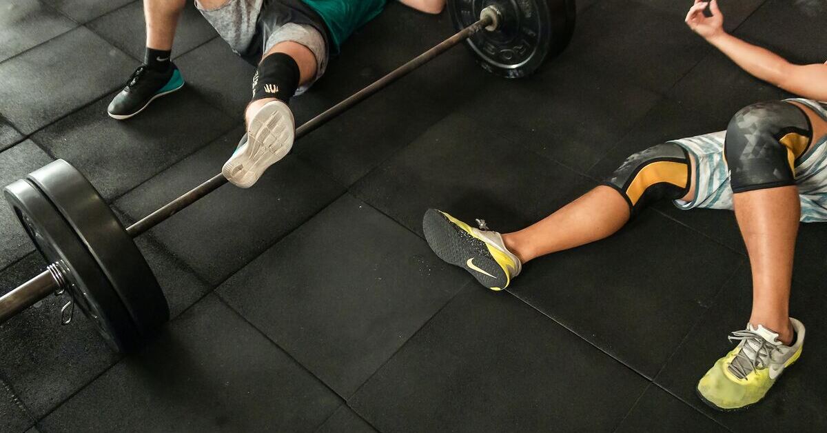 2 lifters lying next to a loaded barbell