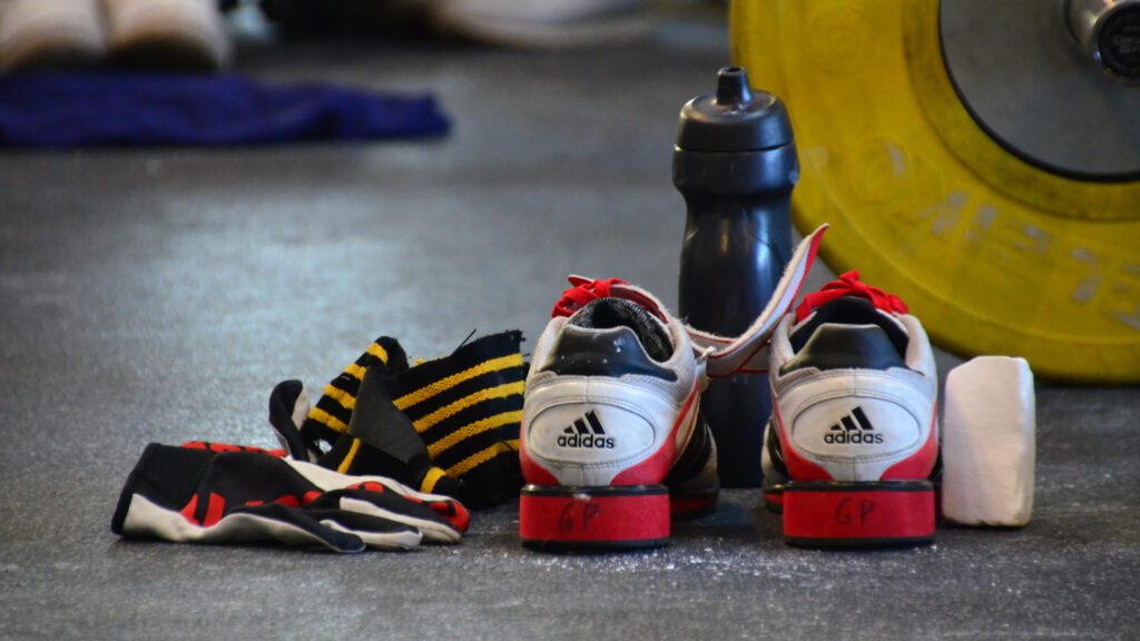 Assorted weight training gear lying on the ground, including a pair of weightlifting shoes
